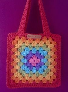 a crocheted bag hanging on a purple wall with a name tag attached to it