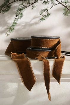 three brown ribbons tied to each other on top of a white surface with pine branches in the background