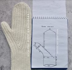 the mitten is next to an open notebook with drawings on it and a hand knitted glove