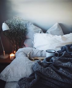 an unmade bed with pillows, blankets and a lamp on the side table next to it