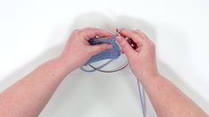 someone is knitting something with their hands on a white surface and they are holding the yarn