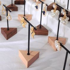 several pairs of earrings are displayed on wooden stands with black metal posts and wood bases