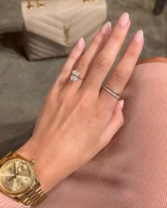 a woman's hand with two different rings on her wrist and a purse in the background