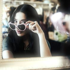 a girl looking at herself in the mirror with her pink heart shaped sunglasses on,