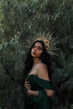 a woman in a green dress with a crown on her head standing next to trees