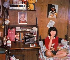 a woman sitting on top of a bed next to a desk with pictures and stuffed animals