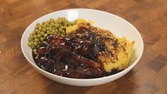 a white bowl filled with meat, mashed potatoes and peas on top of a wooden table