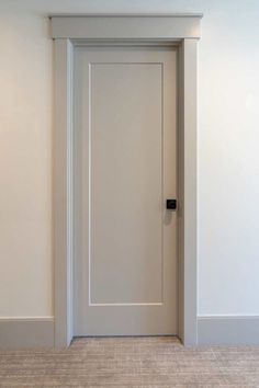 an empty room with a white door and beige carpeted floor is seen in this image