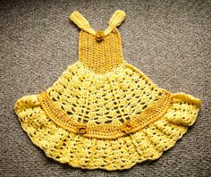 a crocheted yellow dress is laying on the floor next to a gray carpet