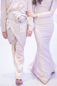 two people walking down a runway wearing white outfits and one is holding the other's hand