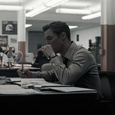 a man sitting at a desk with his hand on his face and looking down while holding a pen