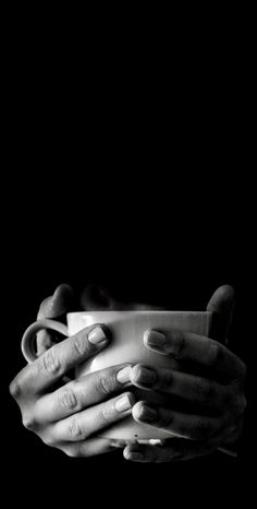 black and white photograph of two hands holding a coffee cup in front of a dark background