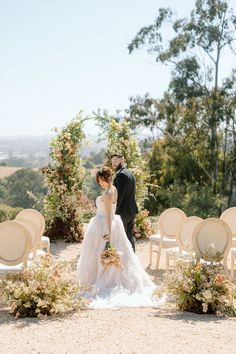 a bride and groom standing in front of an outdoor ceremony set up with white chairs