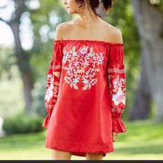 a woman wearing a red dress with floral embroidery on the shoulders and sleeves, looking off to the side