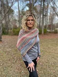 a woman is standing in the grass with her hands on her hips and wearing a knitted shawl