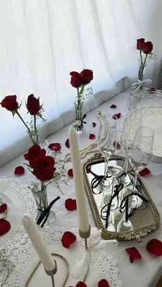 a table topped with candles and flowers on top of a white tablecloth covered in red roses