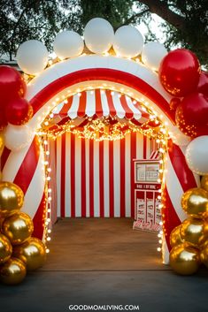 an entrance to a circus with balloons and lights on the sides, in front of a red and white striped tent