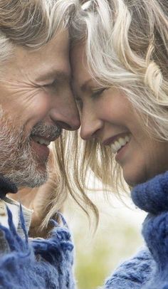 a man and woman smiling at each other with their faces close to one another, both wearing blue sweaters