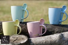 four different colored mugs sitting on top of a log