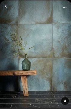 a green vase sitting on top of a wooden table next to a blue tiled wall