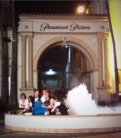 some people are posing for a picture in front of a fountain with water shooting out of it