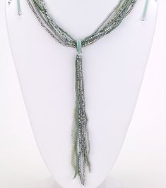 Teal multi-strand beaded necklace on a suede strap featuring a dangle lariat in green teal and gray hues. Elegant Adjustable Green Lariat Necklace, Adjustable Green Lariat Necklace, Adjustable Green Beaded Lariat Necklace, Adjustable Green Bohemian Lariat Necklace, Adjustable Multi-strand Beaded Lariat Necklace, Elegant Turquoise Beaded Lariat Necklace, Green Multi-strand Jewelry With Dangling Beads, Teal And Gray, Multi Strand Beaded Necklace