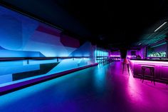 an empty bar with purple and blue lights on the walls, along with stools