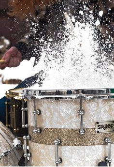 a man is playing drums with snow falling on him and his feet in the air