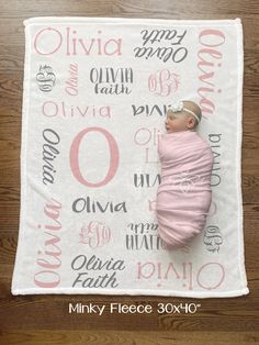 a baby wrapped in a pink blanket laying on top of a wooden floor next to a wall