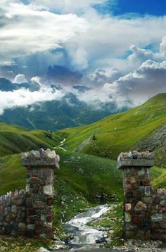 an old stone gate in the middle of a green valley with mountains in the background