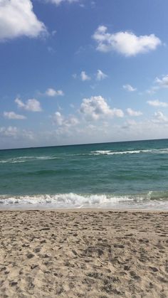 a person is walking on the beach with a surfboard in their hand and there are waves coming in from the ocean