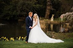 a bride and groom standing next to each other in front of a pond with daffodils