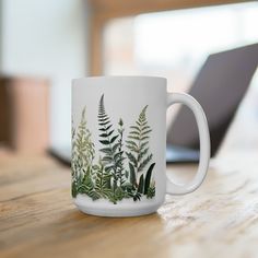 a white coffee mug sitting on top of a wooden table next to a laptop computer