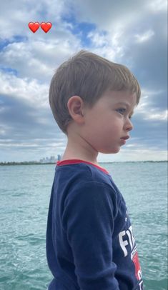 a young boy standing on top of a boat near the ocean with hearts floating in the air