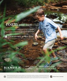 a young boy walking across a river next to a forest