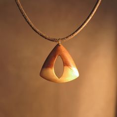 a wooden pendant hangs from a leather cord on a brown background with light coming through the window