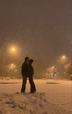 two people standing in the snow at night with their arms around each other looking into the distance