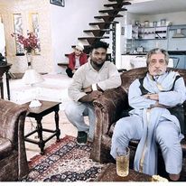 two men sitting on couches in a living room next to a spiral stair case