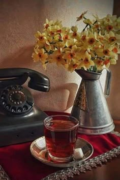 a vase with flowers and a cup on a table next to an old fashioned phone