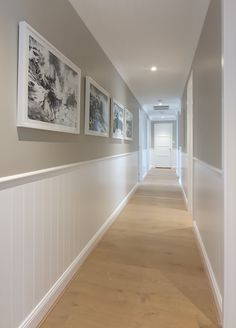 a long hallway with pictures on the wall and wood flooring in front of it