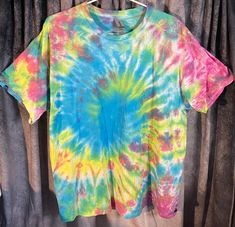 a colorful tie - dyed shirt hanging on a clothes rack with curtains in the background