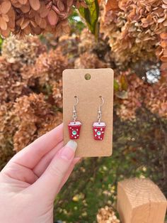 a person holding up a pair of red cup earrings