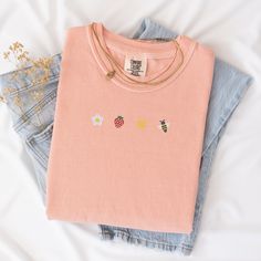 Welcome the sunny days with our Sunkissed Strawberry and Bee Embroidered T-Shirt! Made from 100% cotton Soft Comfort Colors, this shirt is both stylish and comfortable, perfect for your summer adventures.Features:Material: 100% cotton Soft Comfort ColorsSizes: S, M, L, XL, 2XL (refer to size chart in images)Colors Available: Banana, Bay, Blossom, Chalky Mint, Chambray, Ivory, Orchid, Peachy, Violet (Note: Colors may vary slightly due to monitor settings)Design: Summer-inspired embroidery featuring a daisy, strawberry, sun, and bee on the center chestCare Instructions: Machine wash cold, tumble dry lowThis Sunlissed Strawberry and Bee Embroidered T-Shirt is a delightful addition to your wardrobe, bringing a touch of sunshine wherever you go. Perfect for picnics, beach days, or casual outing Cute Embroidered T-shirt For Spring, Pink Summer Tops With Embroidered Graphics, Cute Embroidered Relaxed Fit Tops, Pink Embroidered Summer Top, Cute Embroidered Tops With Relaxed Fit, Pink Embroidered Tops For Summer, Cute Embroidered Summer T-shirt, Cute Embroidered Graphic Tops For Spring, Summer Pink T-shirt With Floral Embroidery