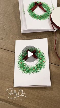 two cards with christmas wreaths on them sitting next to a reel of twine