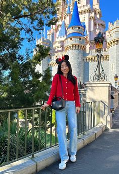 a woman standing in front of a castle with a mickey mouse hat on her head