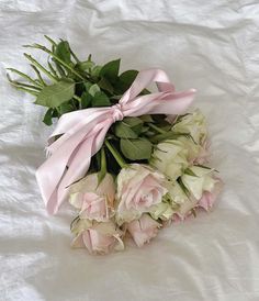 a bouquet of flowers with pink ribbons on a white sheeted bed spread, ready to be used as a decoration