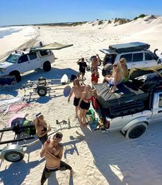 a group of people standing on top of a sandy beach next to cars and surfboards