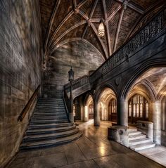 an old building with stone floors and stairs leading up to the second floor that is lit by a chandelier