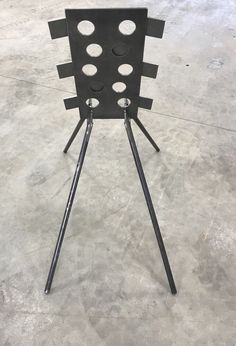 a black chair sitting on top of a metal tripod in a room with concrete floors