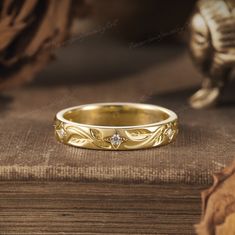 a gold wedding band with three diamonds on top of a wooden table next to a statue